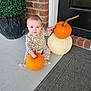 baby, child, pumpkin, orange_pumpkin, white_pumpkin, porch, brick_wall, door, doormat, plant_pot, green_plant, sitting, holding, blue_eyes, cozy_outfit, autumn, fall, cute, curious, indoors