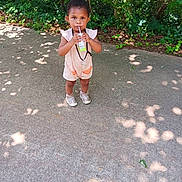 Ahlani joined the competition — help win amazing prizes! casual_clothing, child, concrete, cute, daylight, drinking, greenery, juice_box, nature, outdoor, person, shadows, shoes, sidewalk, standing, summer, sunlight, toddler, trees, young_child