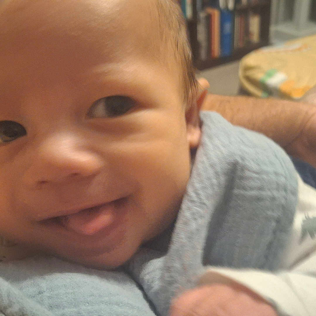 Michael joined the competition — help win amazing prizes! baby, smiling, tongue_out, blanket, indoor, bed, bookshelf, person, face, infant, cute, cozy, child, happy, clothing, portrait, young, family, skin, home