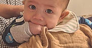 Michael joined the competition — help win amazing prizes! baby, infant, hand, blanket, clothing, face, eyes, indoor, curtain, bed, soft_lighting, chewing, resting, person, cute, young_child, toddler, sleepwear, comfort, holding