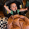 Milo is registered to the contest to win money with this photo: baby, car_seat, blanket, infant, child, indoor, expression, reaching, seat_belt, wood_floor, bag, checkered_pattern, clothing, pink_blanket, person, face, wide_eyes, open_mouth, hand, straps