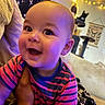 baby, child, smiling, striped_shirt, indoor, person, face, hand, cat, cat_tree, string_lights, home_decor, couch, blanket, happy, portrait, close_up, toddler, furniture, cozy