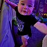 baby, child, playpen, tshirt, diaper, indoor, purple_light, curious, standing, toy, floor, hand, face, person, infant, candid, expression, home, young, reaching