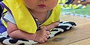 Daniel is registered to the contest to win money with this photo: baby, child, helmet, yellow, vest, indoor, floor, wood, mat, pattern, person, curious, expression, wide_eyes, blurred_background, people, soft, clothing, infant, laying