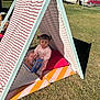 toddler, child, tent, outdoor, grass, cushion, book, pigtails, pink_clothing, sunlight, playtime, reading, fabric, patterned_tent, daylight, park, fun, cute, leisure, young_child