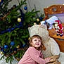 Mylana a rejoint le concours — aidez-le/la à gagner de superbes lots ! blue_baubles, child, christmas_tree, festive, gold_baubles, greenery, happy, holiday_decor, indoor, lights, ornaments, pink_shirt, playful, santa_figurine, smiling, teddy_bear, toddler, winter_scene, wooden_furniture, wooden_sled