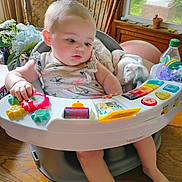 Nevaeh joined the competition — help win amazing prizes! baby, blanket, bottle, child, colorful, curious, face, highchair, home, indoor, infant, pacifier, person, plant, playing, table, toy, window, wooden_chair, wooden_floor