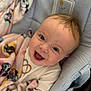 baby, baby_garment, blanket, blue_eyes, child, closeup, clothing, cozy, cute, face, greeting, happy, head, indoor, infant, patterned_blanket, portrait, seated, smiling, soft_texture