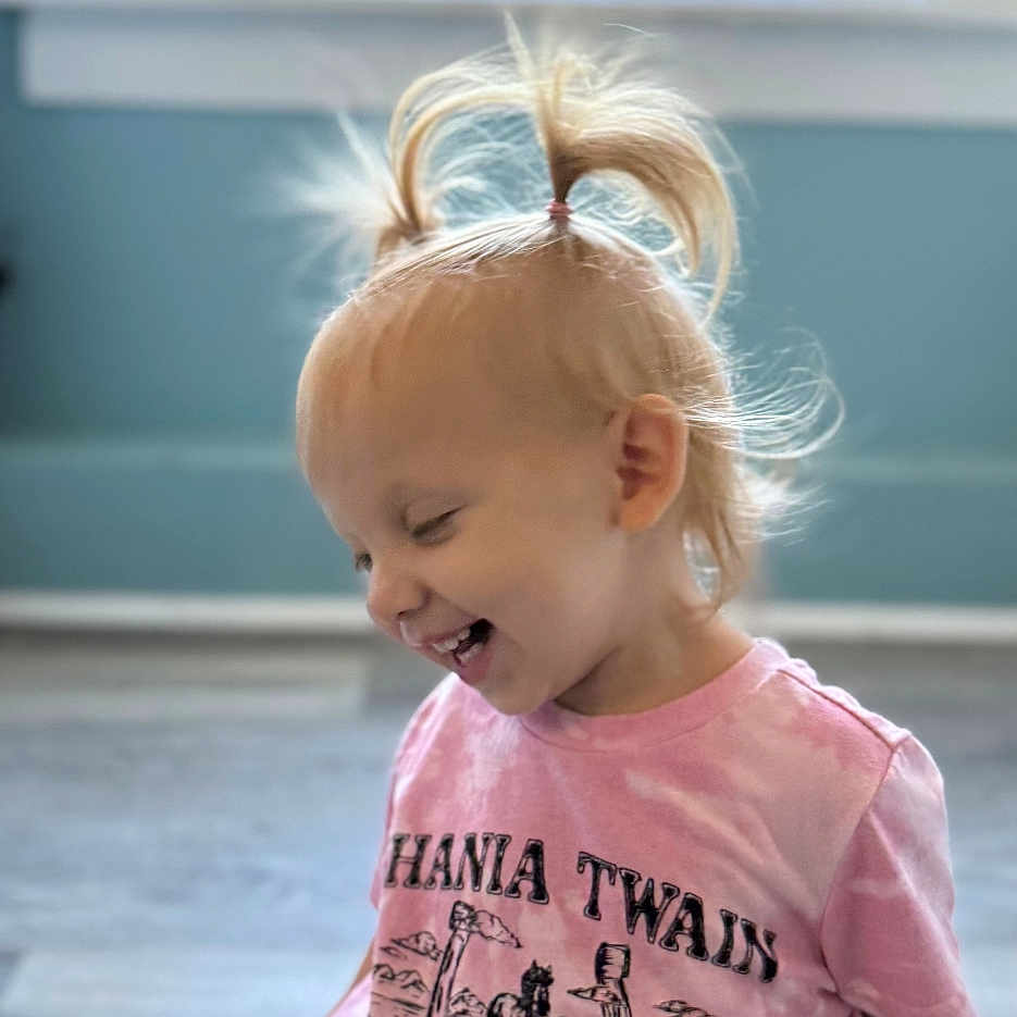 Bailee is registered to the contest to win money with this photo: black_shorts, blonde_hair, casual_clothing, child, cute, floor, happy, home, indoor, laughing, natural_light, pigtails, pink_tshirt, playful, portrait, sitting, smiling, toddler, window, young_child