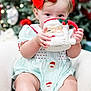 baby, blurry_background, chair, child, christmas, clothing, cute, decorations, face, feet, festive, holding, holiday, holiday_season, indoor, portrait, red_bow, santa_mug, smiling, toddler