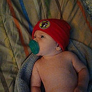 Jayce is registered to the contest to win money with this photo: baby, infant, pacifier, red_hat, blanket, striped_blanket, towel, lying_down, indoors, cute, child, headwear, sleepwear, skin, newborn, resting, young_child, beanie, portrait, baby_boy