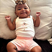 Genesis is registered to the contest to win money with this photo: baby, infant, smiling, bow, headband, white_tank_top, pink_shorts, cushion, couch, indoor, happy, portrait, child, cute, furniture, person, skin, face, baby_clothes, relaxed