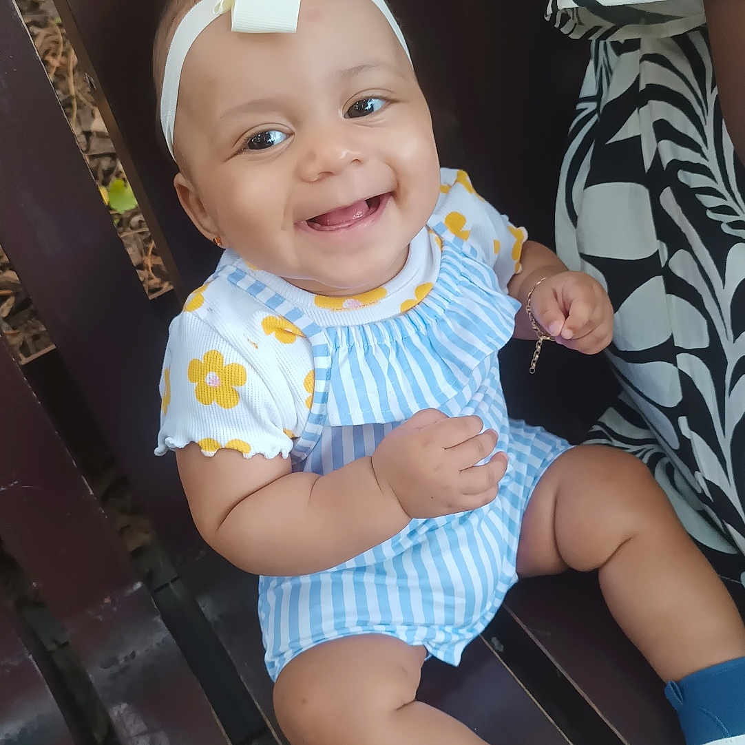 Tayla a rejoint le concours — aidez-le/la à gagner de superbes lots ! baby, bench, blue_shoes, bow, child, cute, eyes, face, hand_bracelet, happy, headband, outdoor, patterned_clothing, person, sitting, smiling, striped_clothing, toes, wood, yellow_flowers