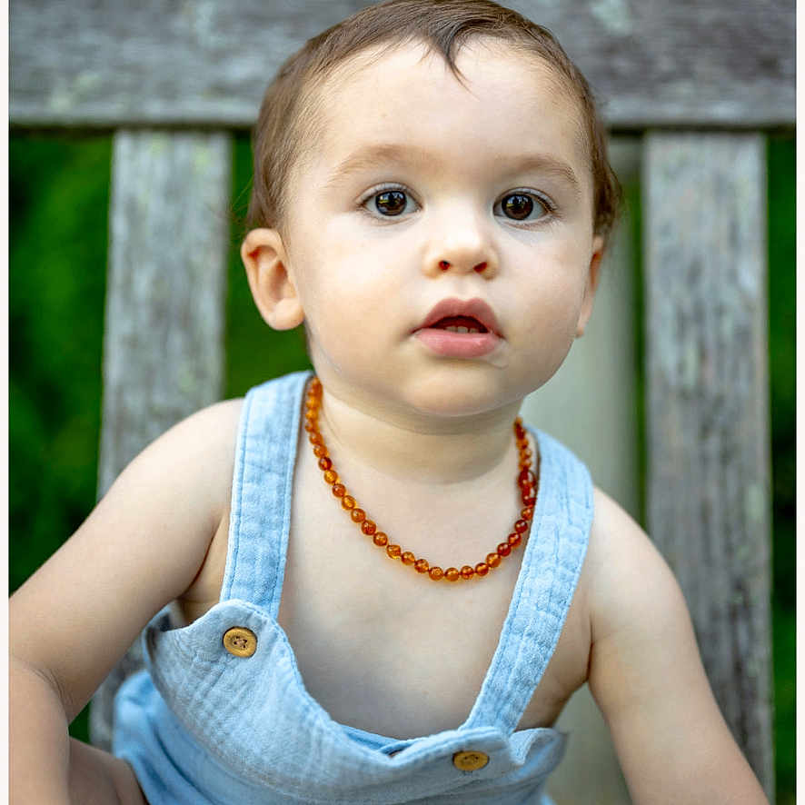 Itai is registered to the contest to win money with this photo: toddler, child, outdoor, bench, overalls, necklace, portrait, greenery, person, young, cute, curious, baby, sitting, wood, nature, casual, summer, expression, innocent