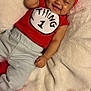 Kulture is registered to the contest to win money with this photo: baby, infant, smiling, red_headband, red_shirt, thing_1, pants, blanket, soft_texture, happy, cute, lying_down, indoors, child, person, headwear, cheeks, dimples, relaxed, cozy