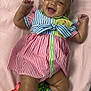 baby, child, smiling, laughing, striped_dress, headband, bow, colorful_clothing, socks, lying_down, pink_background, happy, cute, infant, portrait, indoors, cheerful, fashion, accessory, skin
