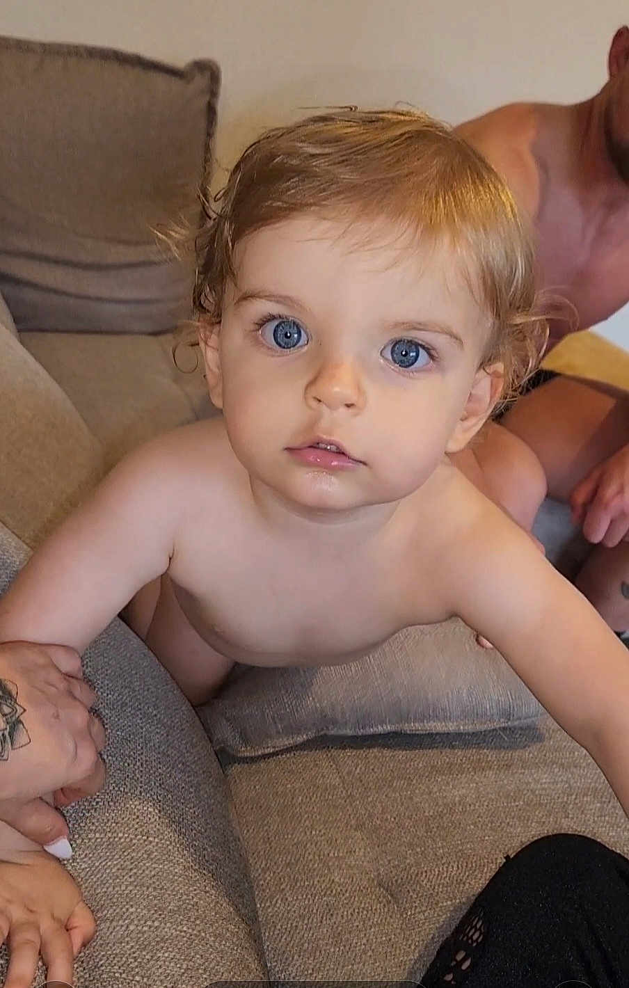 Maé a rejoint le concours — aidez-le/la à gagner de superbes lots ! toddler, child, blue_eyes, blonde_hair, couch, sofa, hand_holding, adult, indoor, curious, climbing, person, skin, face, living_room, tattoo, bare_chest, pillow, close_up, expression