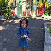 Jayani participe au concours pour gagner de l'argent avec cette photo : child, girl, denim_dress, apple, smiling, pigtails, sandals, outdoor, school, gate, pavement, trees, sunlight, shadow, plants, greenery, happy, daytime, casual, portrait