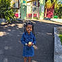 child, girl, denim_dress, apple, smiling, pigtails, sandals, outdoor, school, gate, pavement, trees, sunlight, shadow, plants, greenery, happy, daytime, casual, portrait