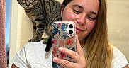 Athena participe au concours pour gagner de l'argent avec cette photo : bathroom, casual, cat, cute, earrings, friendly, indoor, long_hair, mirror, person, pet, reflection, selfie, shoulder, smartphone, smile, tabby_cat, tattoo, white_shirt, woman