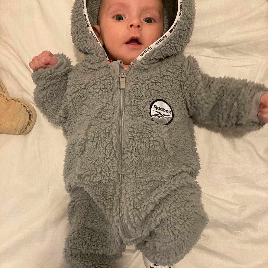 Kassym participe au concours pour gagner de l'argent avec cette photo : baby, bed, blanket, child, cute, eyes, face, fluffy, footwear, gray, hands, hooded_clothing, indoor, infant, lying_down, onesie, person, portrait, socks, soft