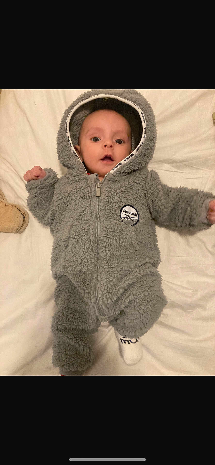 Kassym participe au concours pour gagner de l'argent avec cette photo : baby, child, infant, hooded_clothing, onesie, gray, fluffy, soft, bed, blanket, lying_down, cute, face, eyes, hands, footwear, socks, indoor, person, portrait