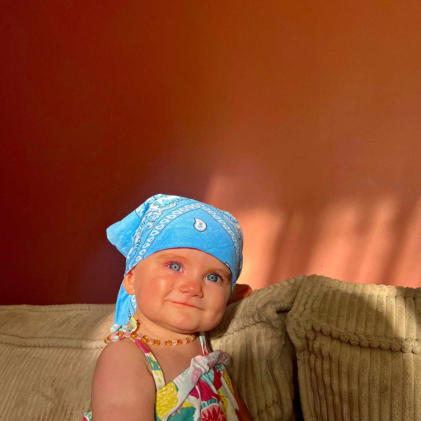 Maïana a rejoint le concours — aidez-le/la à gagner de superbes lots ! baby, beige_couch, blue_bandana, blue_eyes, child, couch, cute, floral_dress, happy, indoor, necklace, person, portrait, shadow, smiling, sunlight, textured_cushion, toddler, wall, warm_light