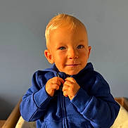 Stanislas a rejoint le concours — aidez-le/la à gagner de superbes lots ! toddler, child, blue_hoodie, blonde_hair, smiling, face, hands, zipping, indoor, portrait, young_child, cute, playful, warm_light, casual_clothing, seated, person, baby, expression, background