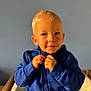 toddler, child, blue_hoodie, blonde_hair, smiling, face, hands, zipping, indoor, portrait, young_child, cute, playful, warm_light, casual_clothing, seated, person, baby, expression, background