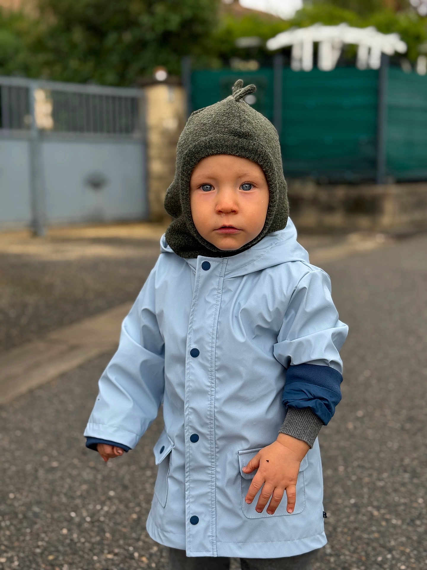 Stanislas a rejoint le concours — aidez-le/la à gagner de superbes lots ! child, toddler, hat, raincoat, blue_jacket, outdoor, street, pavement, face, serious_expression, winter_clothing, knit_hat, person, young_child, portrait, daytime, urban, casual, cute, standing