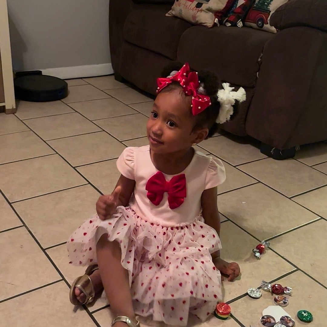 Valeria Gonzalez is registered to the contest to win money with this photo: bow, candy, child, couch, cute, decor, dress, floor, footwear, girl, hair_accessory, home, indoors, living_room, pillow, playful, portrait, sandals, sitting, tile