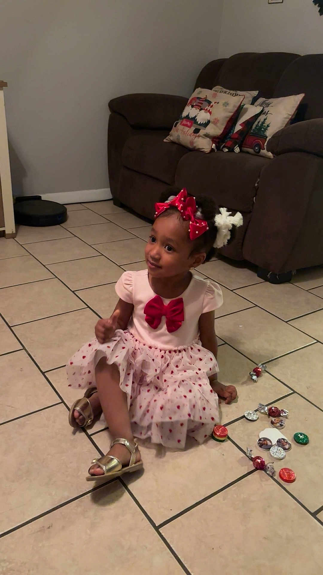 Valeria Gonzalez is registered to the contest to win money with this photo: child, girl, dress, bow, sitting, floor, tile, candy, living_room, couch, pillow, home, indoors, footwear, sandals, hair_accessory, cute, decor, playful, portrait