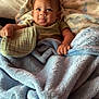 Kaniela-Ray joined the competition — help win amazing prizes! baby, blanket, bed, pillow, knitted_item, child, cozy, soft_texture, indoor, cute, infant, person, portrait, wrapped, fabric, sleeping_area, comfort, young_child, hands, smiling
