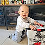 baby, box, cabinet, child, decorations, face, floor, furniture, happy, headphones, home, indoor, kneeling, mickey_mouse, pajamas, person, photo_frame, plant, smiling, toy