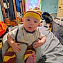 baby, infant, child, indoor, seat, clothing, hat, pants, bib, foot, face, expression, furniture, bed, room, colorful, tie_dye, wooden_wardrobe, basket, blanket