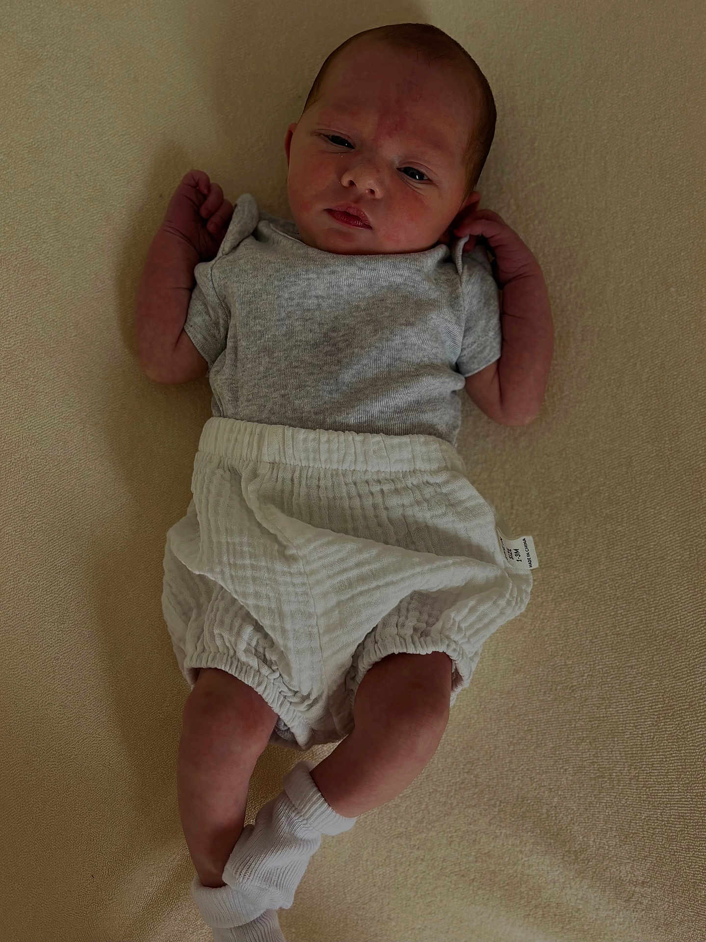 Louise participe au concours pour gagner de l'argent avec cette photo : baby, newborn, infant, clothing, sock, shorts, shirt, lying_down, face, skin, person, cute, portrait, indoors, soft_surface, expression, young_child, small_hands, small_legs, babywear