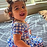 toddler, child, girl, smiling, laughing, portrait, indoor, bedroom, sitting, pajamas, dress, hair_bows, pigtails, curly_hair, window, sunlight, blinds, bed, patterned_blanket, happy