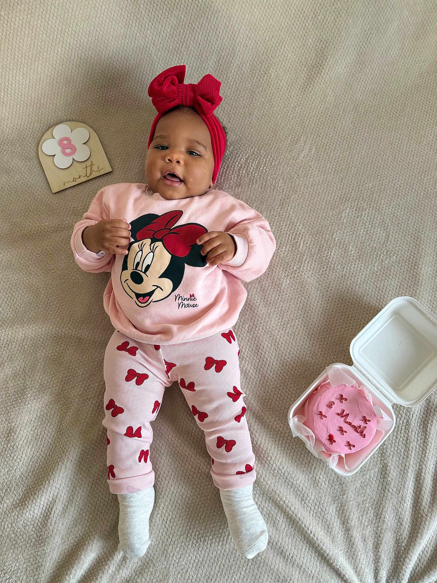 Ellyne a rejoint le concours — aidez-le/la à gagner de superbes lots ! baby, child, infant, pajamas, red_bow, headband, blanket, cake, milestone, 8_months, celebration, pink, smiling, lying_down, cute, clothing, person, indoor, portrait, happy