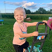 Asher James K Sabat is registered to the contest to win money with this photo: boy, child, clothing, e_scooter, face, grass, happy, head, lawn, male, outdoors, person, photography, plant, portrait, sleeve, smile, tractor, transportation, vehicle