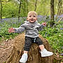 toddler, child, tree_stump, forest, greenery, purple_flowers, hoodie, white_sneakers, nature, outdoor, happy, smiling, sitting, young_child, casual_clothing, daylight, plants, trees, wood, pathway
