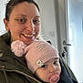 woman, baby, indoor, smile, hat, pacifier, door, keys, jacket, person, face, child, winter_clothing, pom_pom, holding, close_up, portrait, warm_clothing, happy, headwear