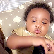Kash is registered to the contest to win money with this photo: baby, child, face, pillow, cushion, bed, blanket, clothing, hand, indoor, person, infant, curly_hair, soft, resting, cute, young, toddler, closeup, skin