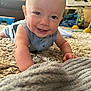baby, smiling, crawling, carpet, blanket, indoor, child, toy, furniture, happy, face, person, blue_clothing, head, eyes, hand, living_room, soft_texture, cute, infant