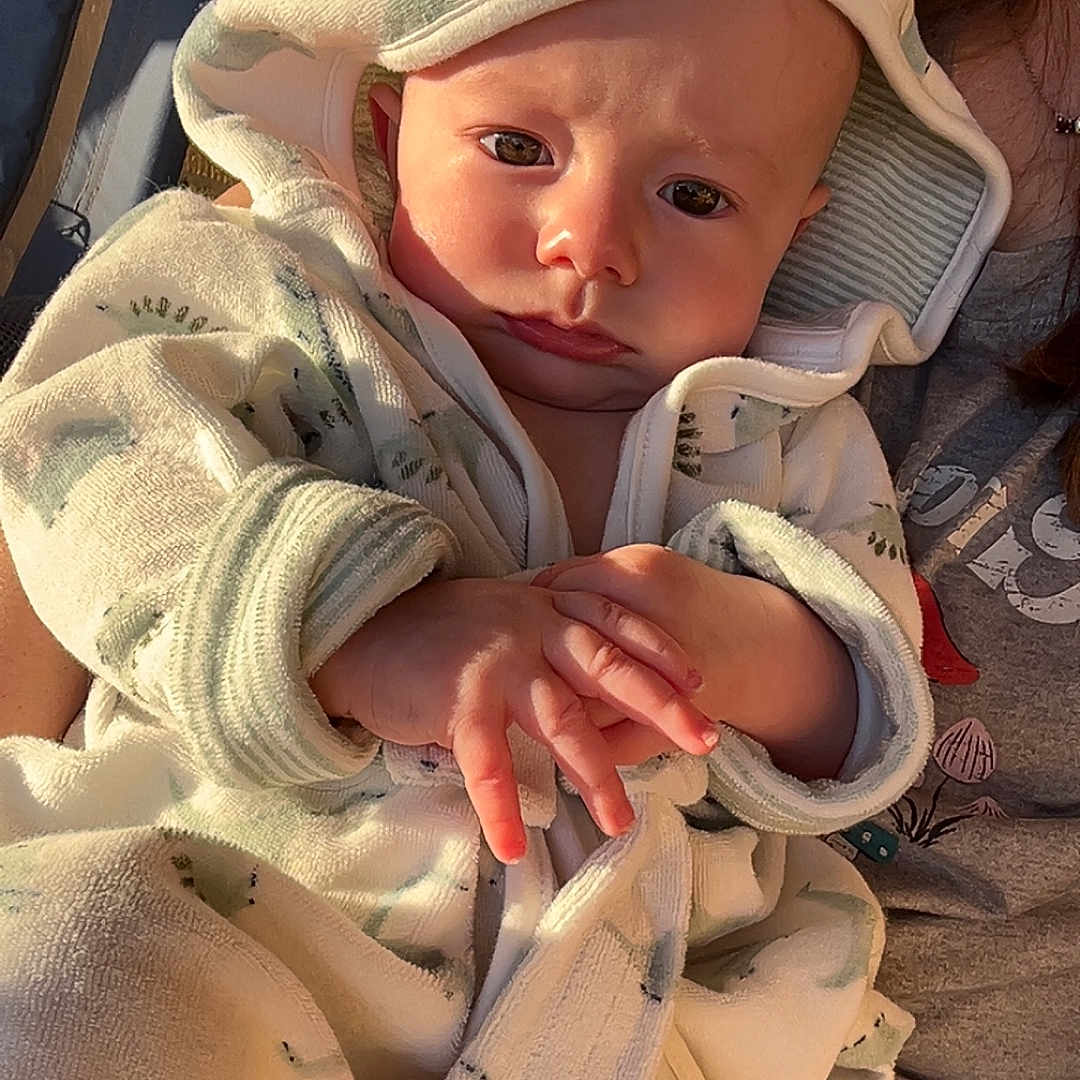 Braxton joined the competition — help win amazing prizes! baby, child, closeup, clothing, cute, dinosaur_pattern, expression, face, hands, hood, human, indoor, infant, person, portrait, robe, sitting, skin, warm_light, young