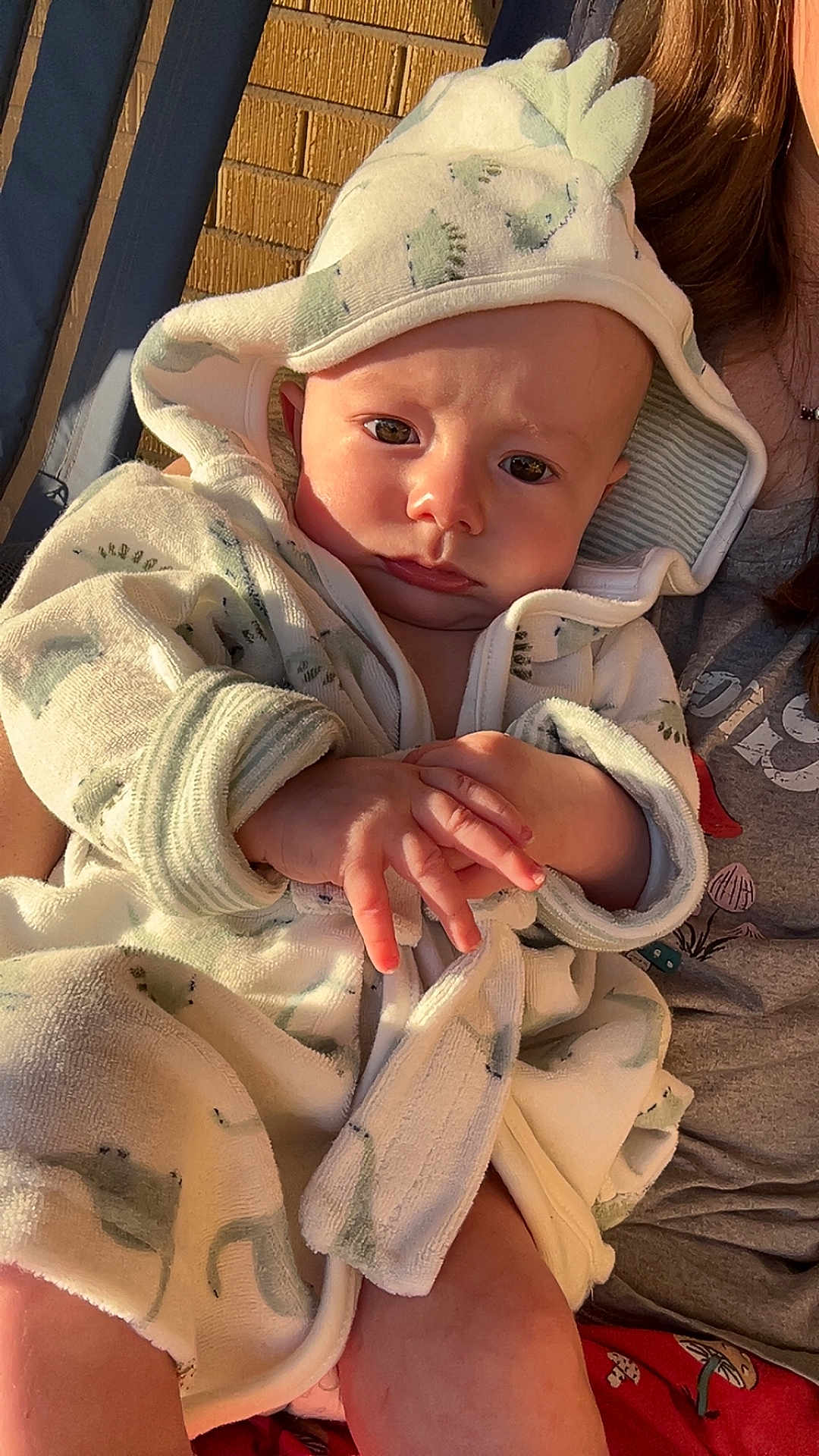 Braxton joined the competition — help win amazing prizes! baby, child, infant, robe, hood, hands, face, person, clothing, warm_light, indoor, closeup, expression, cute, young, skin, human, portrait, sitting, dinosaur_pattern