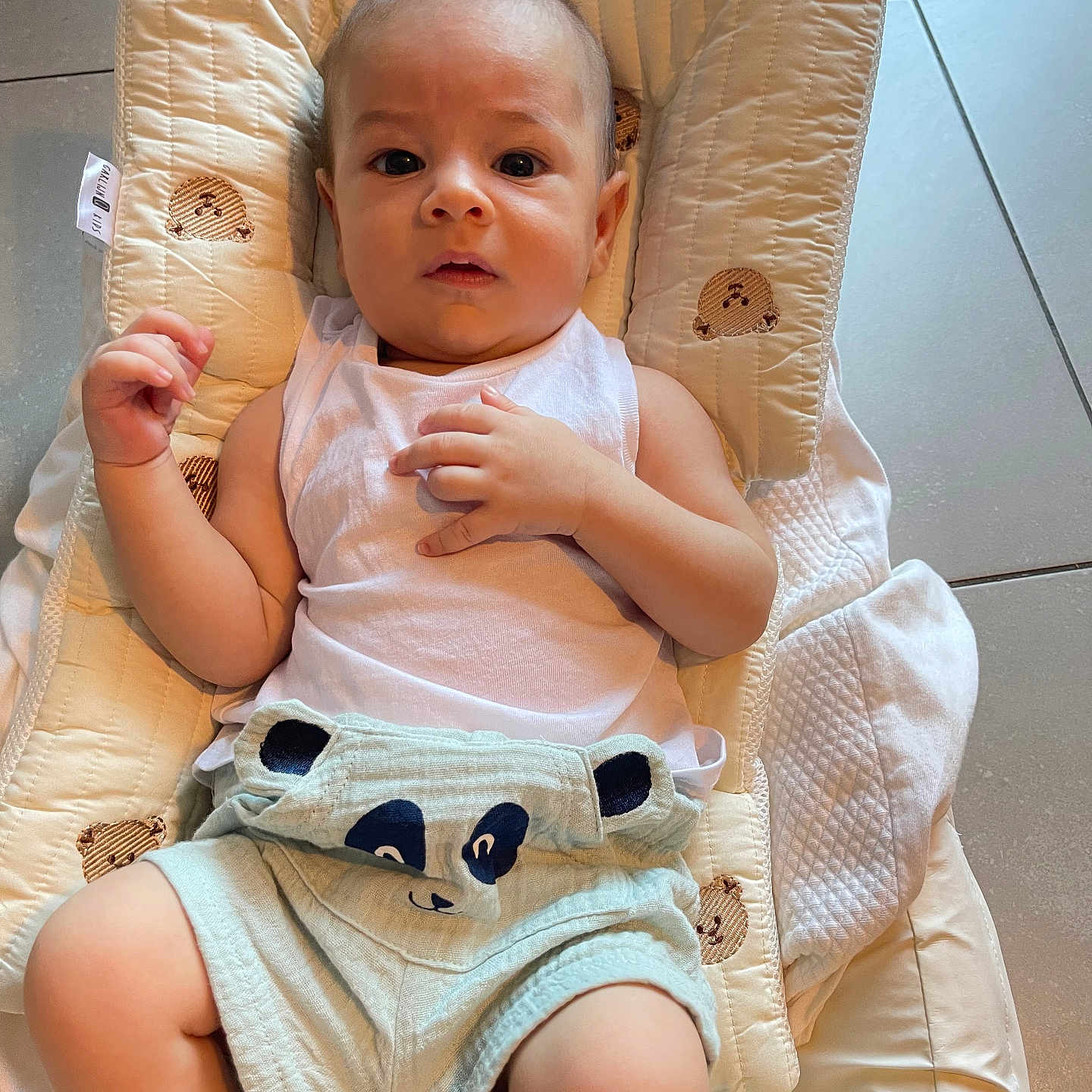 Gabriel a rejoint le concours — aidez-le/la à gagner de superbes lots ! baby, baby_clothes, bear_pattern, child, clothing, cushion, cute, expression, face, floor_tiles, hands, indoor, infant, legs, light, looking_at_camera, panda_shorts, person, soft_toys_pattern, white_tank_top