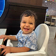 Ali participe au concours pour gagner de l'argent avec cette photo : toddler, child, smiling, high_chair, blue_shirt, leaf_pattern, indoor, restaurant, table, happy, person, face, hair, seat, furniture, cute, baby, expression, joy, hands