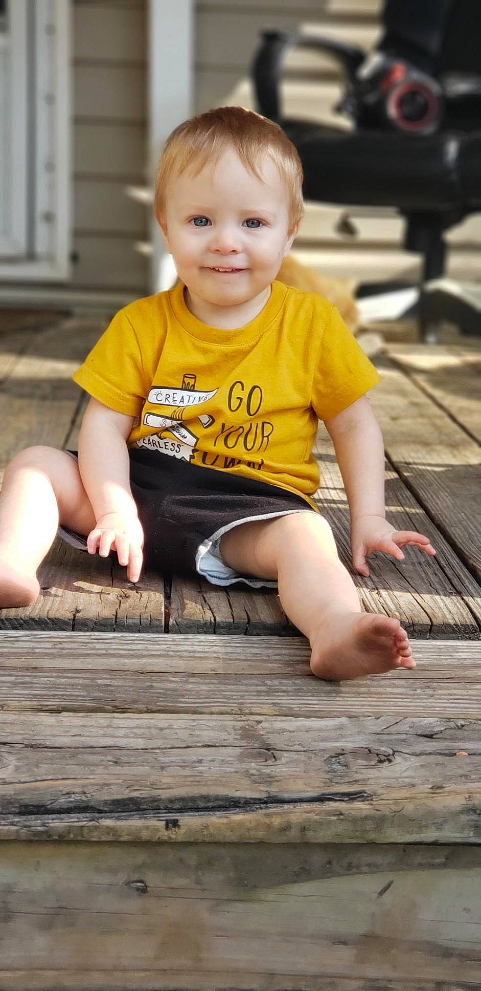 Ryker joined the competition — help win amazing prizes! barefoot, blond, child, child_model, deck, finger, human_body, joy, leg, person, play, shorts, sitting, smile, t_shirt, thigh, toddler, vacation, wood, yellow