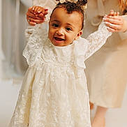 Aivi is registered to the contest to win money with this photo: adult, baby, bows, child, closeup, curly_hair, cute, footwear, hands, happy, indoor, lace, light_skin, people, portrait, smiling, supporting, toddler, walking, white_dress