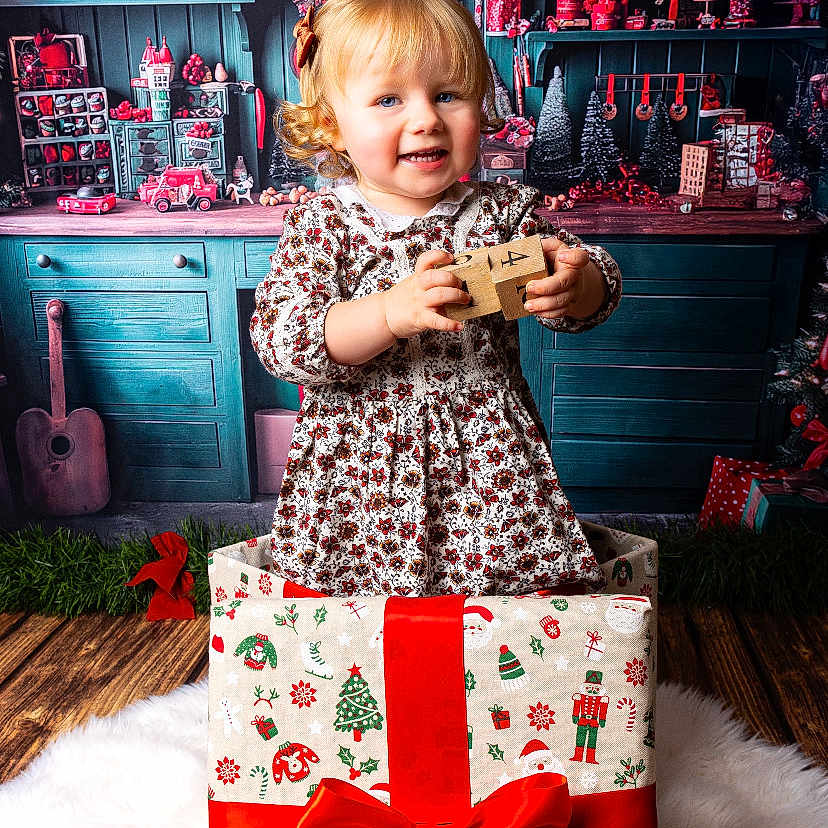 Tahys participe au concours pour gagner de l'argent avec cette photo : celebration, child, christmas, curly_hair, festive_decor, floor_rug, gift_box, happy, holiday, holiday_theme, indoor, miniatures, patterned_dress, red_bow, shelf, smiling, toddler, toys, warm_lighting, wooden_blocks